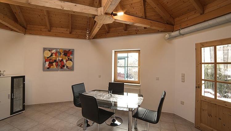 Ein moderner Essbereich mit einem runden Glastisch und schwarzen Stühlen. Die Holzbalkendecke sorgt für eine warme Atmosphäre.