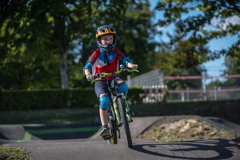 Ein Junge fährt auf einem Fahrrad in einem Park. Er trägt einen Helm und Schutzausrüstung, während er eine Strecke durchquert.