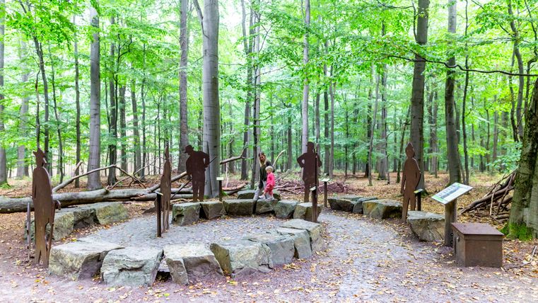 Eine Frau und ein Kind laufen durch einen spiralförmigen Weg, am Rand Skulpturen von Menschen 