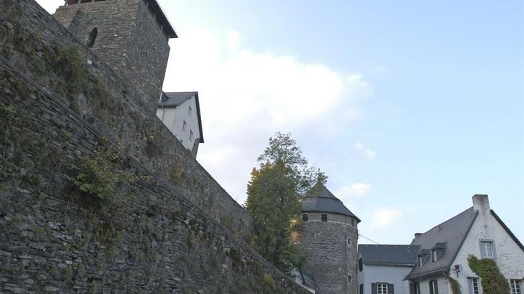 Ein historisches Gebäude mit einer mächtigen Steinmauer und einem Aussichtsturm. Im Hintergrund sind weitere Gebäude und Bäume zu sehen.