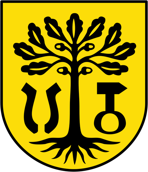Ein Wappen mit einem schwarzen Baum auf gelbem Hintergrund. Unter dem Baum sind verschiedene Symbole zu sehen, die möglicherweise lokale Bedeutung haben.