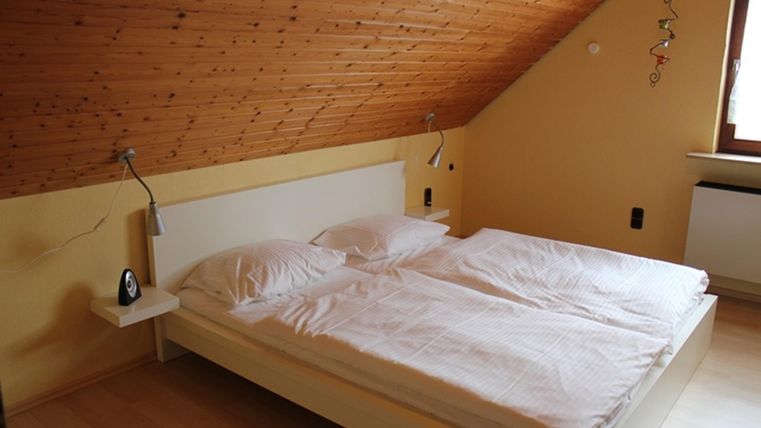 Ein gemütliches Schlafzimmer mit einem Doppelbett und schlichten Nachttischen. Die Wände sind in sanften Farben gehalten und das Dach hat eine Holzverkleidung.