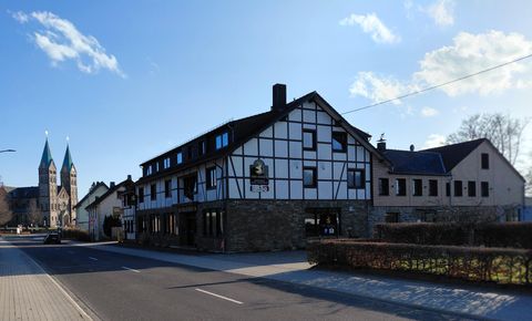 Ein charmantes Fachwerkhaus mit einem Straßencafé. Im Hintergrund sind zwei spitze Kirchtürme sichtbar.