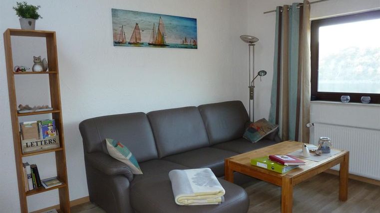 Ein gemütliches Wohnzimmer mit einem grauen Sofa und einem Holztisch. An der Wand hängt ein Bild mit Segelbooten.
