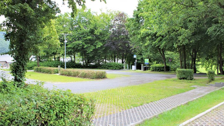 Eine ruhige Parklandschaft mit viel Grün und Bäumen. Der Weg ist mit Pflastersteinen gestaltet und führt durch die Anlage.