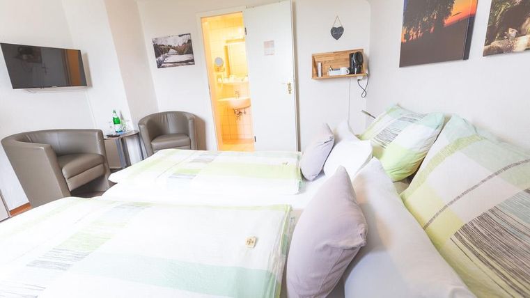 Ein gemütliches Zimmer mit zwei Betten und hübscher Dekoration. Im Hintergrund sind ein Fernseher und ein Badezimmer zu sehen.