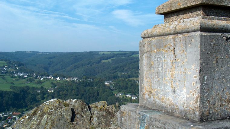 Blick von einem steinernen Denkmal auf eine grüne Landschaft mit einem Dorf im Hintergrund.