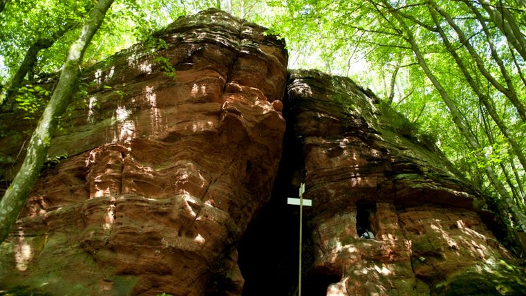 Felsformation mit Höhle im Wald, von Bäumen umgeben.