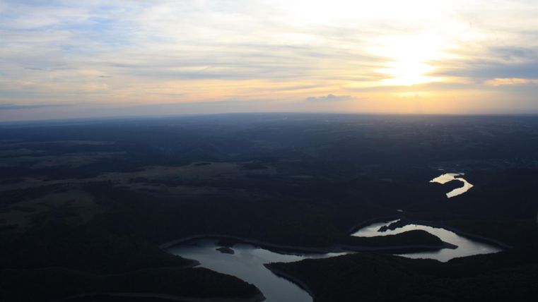 Ein schöner Blick auf einen Fluss, der sich durch die Landschaft schlängelt. Die Sonne geht am Horizont unter und erleuchtet den Himmel.