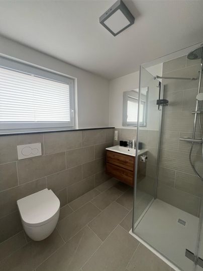 Ein modernes Badezimmer mit einer Dusche aus Glas und einem stilvollen Waschbecken. Die Wände sind in neutralen Farben gehalten, und es gibt ein Fenster für Tageslicht.