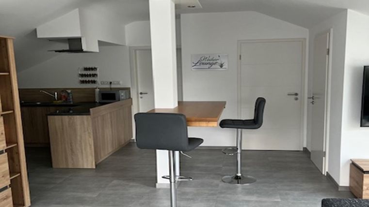 Eine moderne Küche mit Essbereich und Barhockern. Der Raum hat helle Wände und einen offenen, einladenden Charakter.