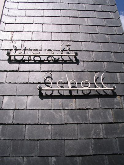 Ein schwarzes Dach mit zwei neonartigen Schildern. Eines zeigt den Schriftzug "Uhr" und das andere "Scholl".