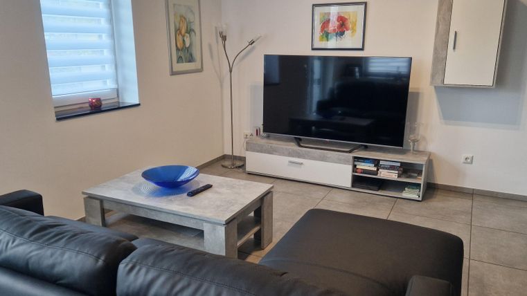 Ein modernes Wohnzimmer mit einem großen Fernseher und einem eleganten Couchtisch. Die Wände sind hell und es gibt einige dekorative Elemente.