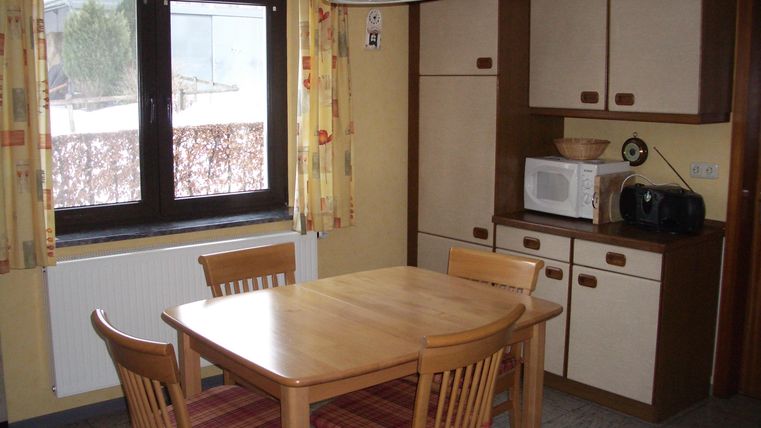 Eine gemütliche Küche mit einem Holztisch und Stühlen. Im Hintergrund sind ein Fenster und einige Küchenschränke sichtbar.