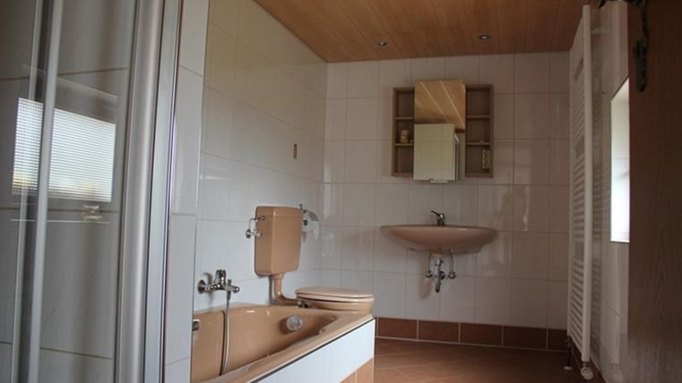 Ein modernes Badezimmer mit einer Badewanne, einem Waschbecken und einer Toilette. Die Wände sind hell gefliest und es gibt einen Holzdecken mit integrierter Beleuchtung.