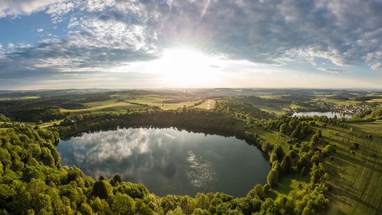 Luftaufnahme von zwei Maaren in einer grünen Landschaft bei Sonnenuntergang.