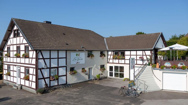 Ein modernes Fachwerkhaus mit einer Terrasse und Blumenfenstern. Es gibt einen klaren blauen Himmel und einen kleinen Fahrradständer.