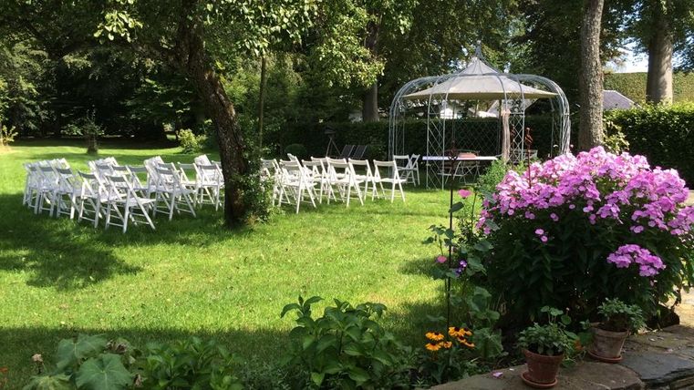 Ein schöner Garten mit weißen Stühlen und einem Pavillon. Bunte Blumen schmücken den Vordergrund.