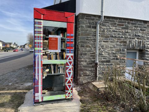 Eine bunte Buchbox steht an der Straßenecke neben einem Gebäude. Sie ist mit verschiedenen Büchern gefüllt und bietet Lesemöglichkeiten für Passanten.