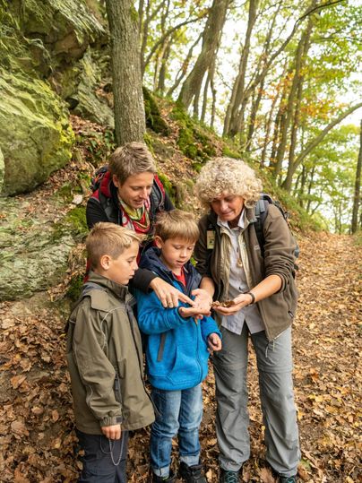 Eine Waldführerin zeigt einer Familie etwas.