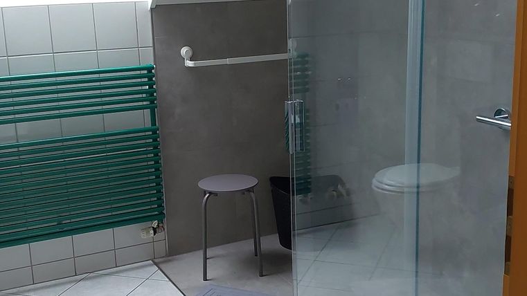 Ein modernes Badezimmer mit einer Glasdusche und einem kleinen Hocker. Der Raum hat eine helle, freundliche Atmosphäre.