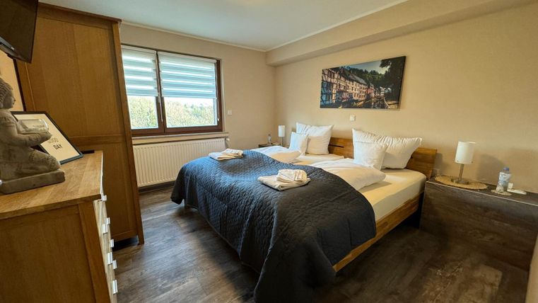 Ein gemütliches Schlafzimmer mit einem großen Bett und modernen Möbeln. Die Wände sind in sanften Farben gehalten und große Fenster lassen viel Licht herein.