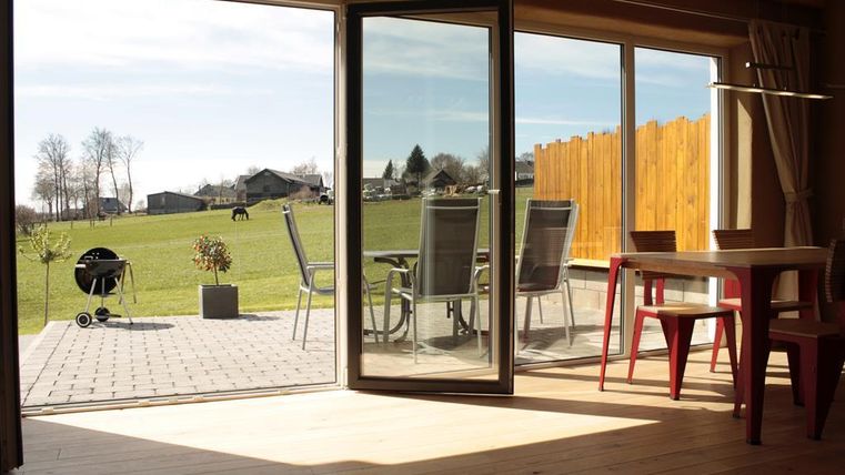 Ein einladender Innenraum mit Blick auf eine grüne Wiese und Häuser im Hintergrund. Draußen stehen Stühle und ein Grill bereit.