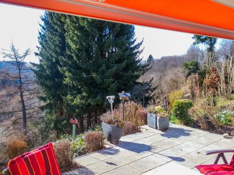 Eine Terrasse mit roten Stühlen und Blick auf eine bewaldete Landschaft. Die Sonne scheint und der Himmel ist blau.