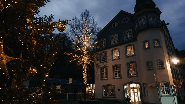 Ein schön beleuchtetes Gebäude zur Weihnachtszeit, umgeben von festlicher Dekoration. Im Vordergrund steht ein geschmückter Weihnachtsbaum.