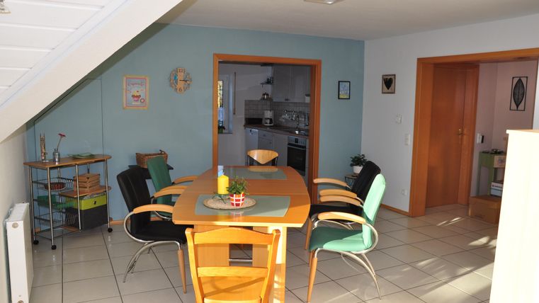 Ein heller Essbereich mit einem runden Tisch und bunten Stühlen. Im Hintergrund ist eine moderne Küche sichtbar.