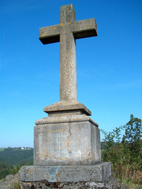 Steinkreuz auf einem Sockel vor blauem Himmel.