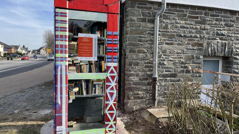 Eine bunte Buchbox steht an der Straßenecke neben einem Gebäude. Sie ist mit verschiedenen Büchern gefüllt und bietet Lesemöglichkeiten für Passanten.