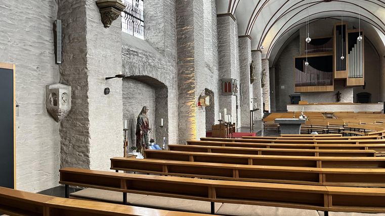 Eine ruhige Kirche mit Holzbänken und einer hohen Decke. An der Wand sind religiöse Statuen und Fenster zu sehen.