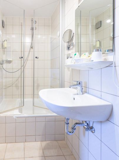 Ein modernes Badezimmer mit einer geräumigen Dusche und einem Waschbecken. Die Wände sind gefliest und die Einrichtung ist hell und schick.