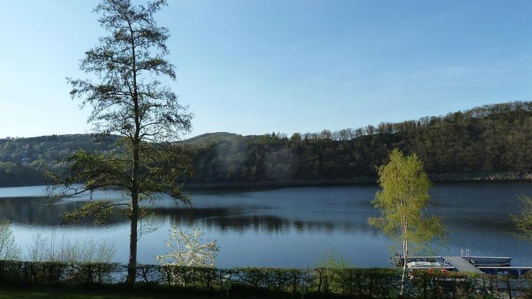 Ein ruhiger See umgeben von Bäumen und sanften Hügeln. Die Landschaft ist friedlich und einladend.
