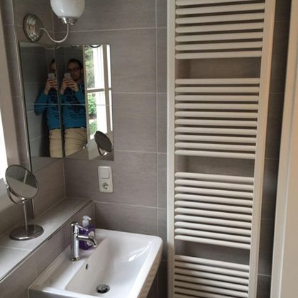 Ein modernes Badezimmer mit einem Waschbecken und einem Handtuchheizkörper. Ein Spiegel und eine Lampe sind ebenfalls sichtbar.