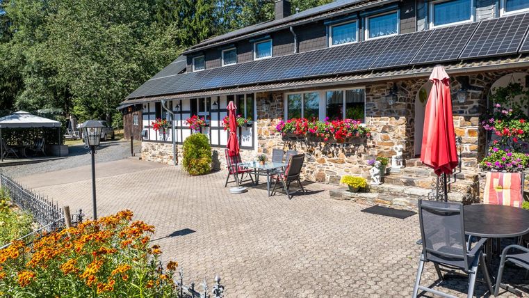 Ein charmantes Haus mit einer Steinfassade und vielen bunten Blumen. Bereich mit Sitzgelegenheiten und Sonnenschirmen im Freien.