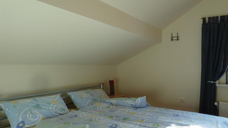 Ein Schlafzimmer mit einem Doppelbett und blauen Bettwäsche. Der Raum hat eine schrägen Decke und ein Fenster mit Vorhängen.