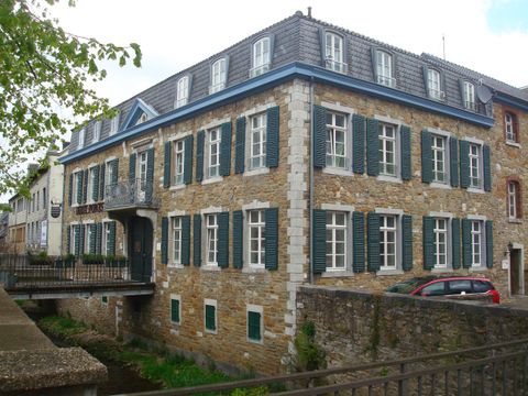 Ein historisches Gebäude mit Steinfassade und vielen Fenstern. Das Dach ist grau und die Fensterläden sind grün.