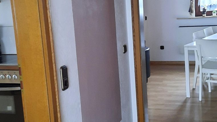 Ein helles Interieur mit einem Flur und Holztüren. An der Wand hängen Garderobenhaken, und der Boden ist mit Teppich ausgelegt.