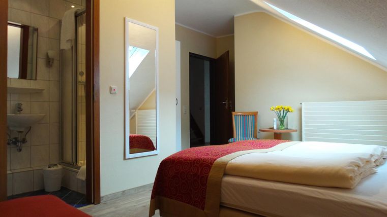 Ein gemütliches Zimmer mit einem Doppelbett und einer Dusche. Sonnenlicht strömt durch das Fenster und sorgt für eine einladende Atmosphäre.