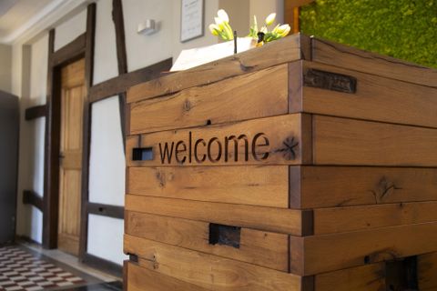 Ein Empfangstresen aus Holz mit der Aufschrift "welcome". Im Hintergrund ist eine lebendige Pflanzenwand zu sehen.