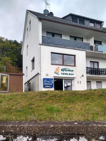 Ein modernes Gebäude mit einem eBike-Verleih. Die Fassade hat große Fenster und einen Balkon.