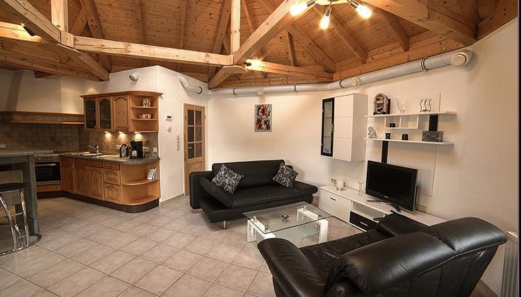 Moderne Wohnung mit Holzdecke und einer gemütlichen Sitzecke. Die offene Küche ist mit Holzschränken und modernen Geräten ausgestattet.