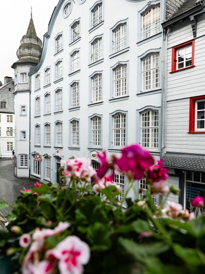 Eine charmante Architektur mit hellblauen Fassaden und vielen Fenstern. Im Vordergrund blühen bunte Blumen.