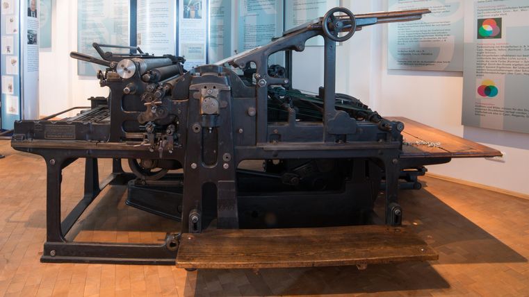 Eine alte Druckmaschine steht in einem Museum. Sie ist in dunkler Farbe gehalten und zeigt mechanische Details.