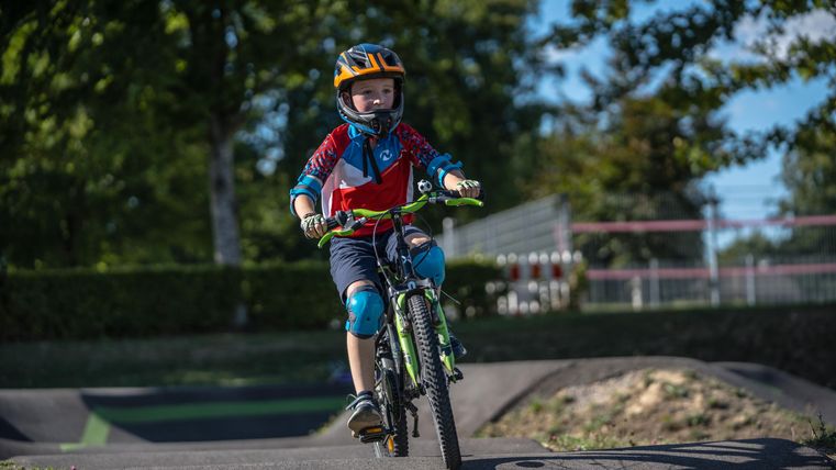 Ein Junge fährt auf einem Fahrrad in einem Park. Er trägt einen Helm und Schutzausrüstung, während er eine Strecke durchquert.