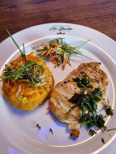 Ein Teller mit gegrilltem Hähnchenbrustfilet, serviert mit pürierten Süßkartoffeln und frischem Gemüse. Die Speisen sind mit Kräutern garniert und schön angerichtet.