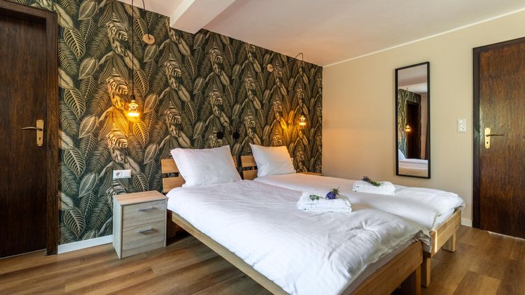 Ein modernes Schlafzimmer mit zwei Einzelbetten und einer grünen Pflanzenwand. Die warmen Lichtquellen schaffen eine gemütliche Atmosphäre.