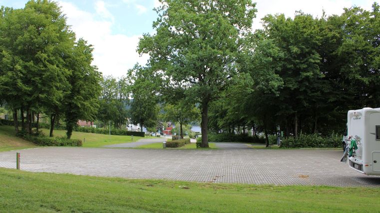 Ein ruhiger Platz mit grünem Rasen und großen Bäumen. Ein Wohnmobil steht in einer geschützten Umgebung.